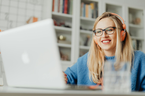 A person wearing orange headphones and glasses smiles while looking at a laptop.